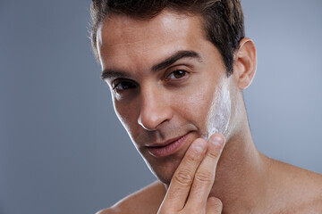 Portrait, cream and man with skincare, glow and moisture on a grey studio background. Face, person...