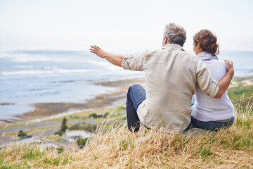 Old couple and pointing at nature on holiday, vacation or embrace with love or support in retirement. Back, man and woman together sightseeing on hill at beach or relax in environment and adventure