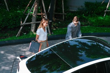 Young couple travel with EV electric car charging in green sustainable city outdoor garden in...