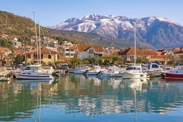 Fototapeta na wymiar Beautiful winter Mediterranean landscape. Montenegro, Tivat city. Marina Kalimanj and fishing boats in harbor. Snow-capped Lovcen mountains