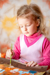 cute baby girl with blond hair is engaged in drawing
