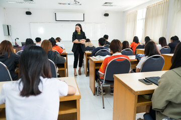 Rearview of university students listen to lecturer explaining lesson in the classroom