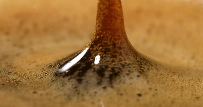 Super slow motion extreme macro of hot creamy aromatic espresso coffee  drop is splashing in transparent mug before being served to customer at cafe or bar at 1000 fps.