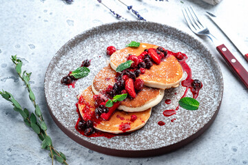 Sweet pancakes with jam and wild berries in a gray plate decorated with powdered sugar and mint, close up
