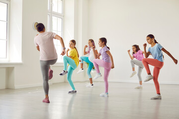 Group of children at dance class. Kids doing sports exercises with professional trainer. Little girl dancers rehearse dynamic moves together with teacher in white room at dance school or youth center