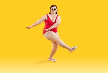 Fototapeta na wymiar Full body portrait of a funny young happy woman in red swimsuit going on summer holiday trip and having fun on a yellow studio background with copy space. Vacation and travel concept.