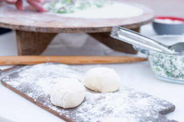Front view of dough for pita. taco lying on wooden board dusted with flour, being rolled out outdoor. Concept of cooking.