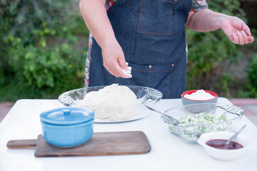 Close up of woman in blue apron kneading dough, making, rolling, buns, putting filling, pouring sauce. Concept of baking.