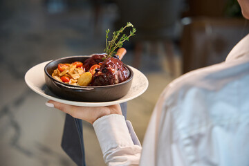 Waitress serves meat with vegetables in a serving pan
