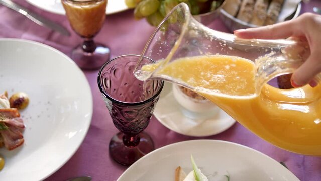 Close-up of orange juice pouring from a jug into a glass . A healthy breakfast made from natural ingredients