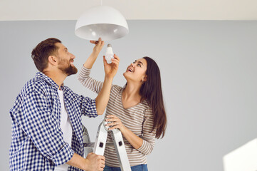 Happy young family couple changing a light bulb together. Cheerful, smiling man and woman standing...