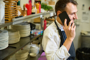 Cook in a chefs apron communicates on his mobile phone - obrazy, fototapety, plakaty