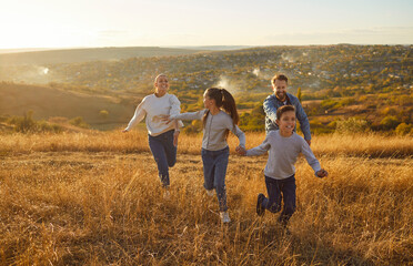 Happy smiling family with two kids daughter and son walking outdoors enjoying beautiful nature. Mother, father with children running outdoors in the field at sunset. Family leisure concept.