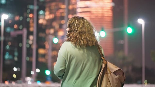 Woman with backpack walking in night city megapolis among skyscrapers in UAE.