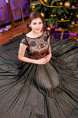 Fototapeta premium Top view, portrait of a young woman in an elegant dress sitting near a Christmas tree.