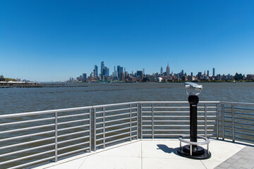 Panoramic view from Hudson River Waterfront Pier in Jersey City, NJ, USA with observation binoculars towards Midtown Manhattan, New York City with skyline of skyscrapers on other side of Hudson river
