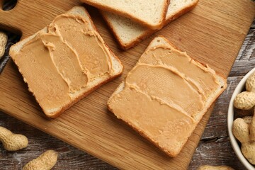 Tasty peanut butter sandwiches and peanuts on wooden table, flat lay