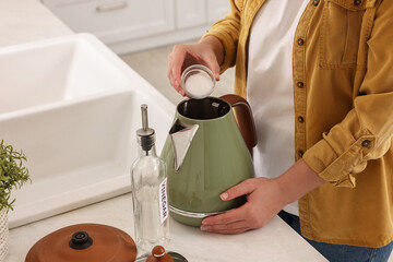 Woman adding baking soda into electric kettle in kitchen, closeup