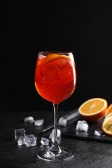 Glass of tasty Aperol spritz cocktail with orange slices and ice cubes on table against black background
