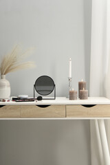 Dressing table with mirror, cosmetic products and burning candles in makeup room