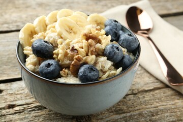Tasty oatmeal with banana, blueberries and walnuts served in bowl on wooden table, closeup