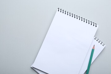 Notebooks and pencil on light grey background, top view. Space for text