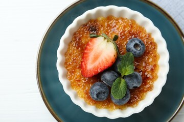 Delicious creme brulee with berries and mint in bowl on white table, top view