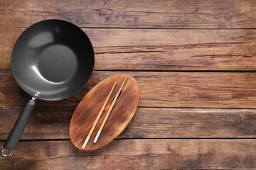 Obraz na płótnie Canvas Empty iron wok and chopsticks on wooden table, flat lay. Space for text