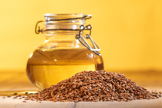Organic flaxseed oil in glass jar with whole flaxseeds on vibrant orange background