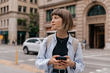 Profile portrait of stylish photo with smartphone looking aside on blurred background in the city 