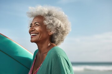 Fototapeta premium Side view, a happy 79-year-old black woman, with surfboard, at beach, teal clothes , in a commercial photography style