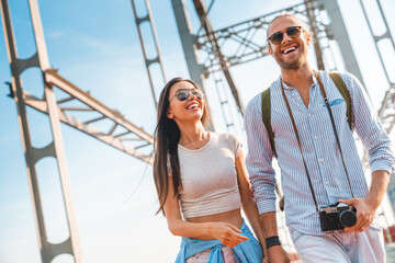 Shot of playful happy young couple holding hands while walking on the bridge outdoors. Caucasian...