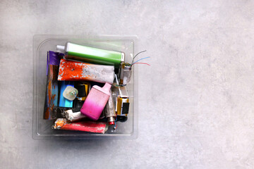 Multi-coloured discarded electronic cigarette vapes placed in a clear plastic tub over a grey...