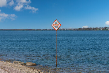 View over a large body of water with in front on shore a warning sign on a post advising of danger and to keep away from the suction intake