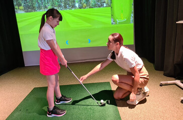Athletic woman trainer teaches teenage girl child to play golf concept. Indoor golf lessons