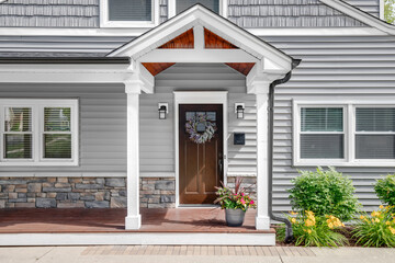 A grey modern farmhouse front door with a covered porch, wood front door with glass window, and grey vinyl and wood siding. - obrazy, fototapety, plakaty