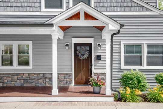 A grey modern farmhouse front door with a covered porch, wood front door with glass window, and grey vinyl and wood siding.