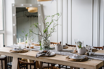 Setting table for Easter dinner with candle, ceramic plates with easter eggs in nest, bunny made of linen napkin. Holidays celebration concept. Decor with vase with twig, branch, leave at home. Set up