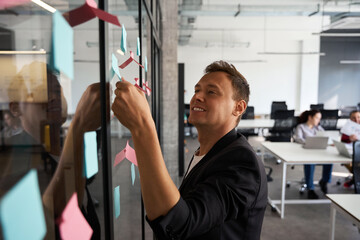 Male lawyer smiling finding memo note with idea stickered on transparent wall