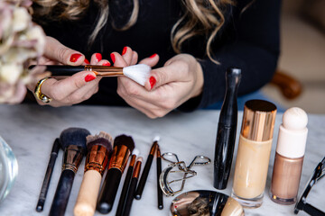 Hands of a makeup artist choosing a brush among a variety of high-end beauty products laid out on a marble surface.