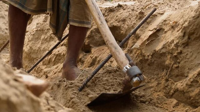 Indian laborer digging lang with traditional Indian shovel in slow motion. Traditional Indian construction. 4K. Indian worker digging a ditch. Iron rod sticking out from the ground. 