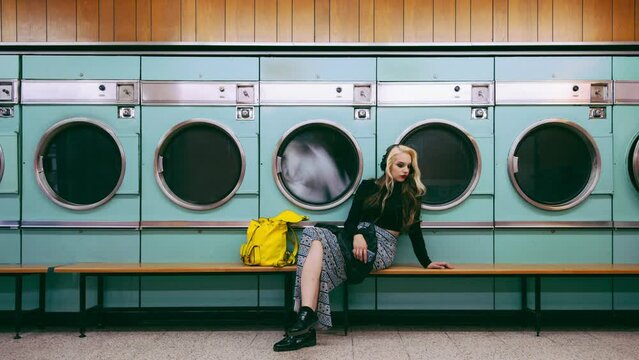 Laundromat for clothes, woman waiting and cleaning service with fashion, style and listening to sad music by washing machine. Young, trendy person or retro model by vintage laundry or spinning effect