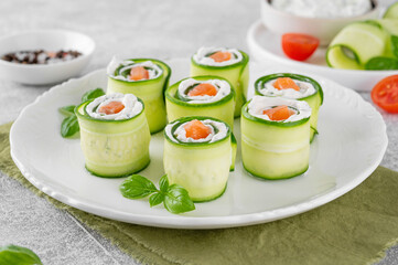 Cucumbers rolls with cream cheese, salted salmon and fresh herbs served on a white plate on a concrete background. Selective focus
