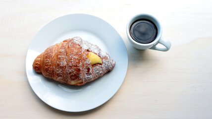 croissant stuffed with cream and cup of coffee on wooden table, natural light