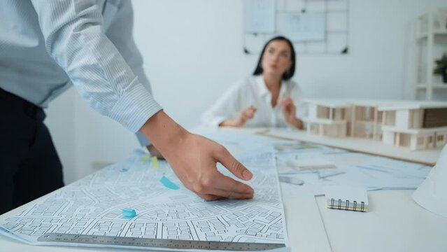 Skilled caucasian interior designer working with house model while discussing with asian architect engineer about house plan on meeting table with blueprint and house model scatter around. Immaculate.