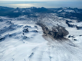 Fototapeta premium A glacier flows towards the Cook Inlet from Mount Iliamna at Lake Clark National Park in Alaska. Rugged and remote glacier with moraine and glacial blue ice. 