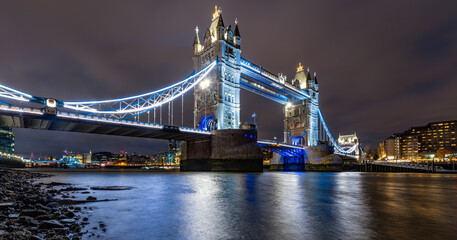 Fototapeta na wymiar Tower Bridge night time panorama in London. Iconic landmark spanning over river Thames at with colorful illumination. Monument, sight and tourist attraction in british metropole from river bank.