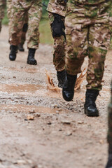 Close up photo, the resilient legs of elite soldiers, clad in camouflage boots, stride purposefully along a hazardous forest path as they embark on a high-stakes military mission