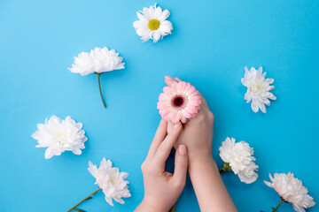 Top view beautiful sophisticated woman hands with white flowers on blue background. Concept organic...