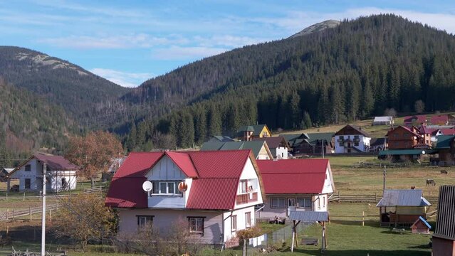 Panoramic view of the Autumn Carpathian Mountains, Cottage Houses on a Sunny Day. Countryside. Hills, forest, garden. Picturesque view of the roofs of houses, meadows. Ski resort in Bukovel, Ukraine.